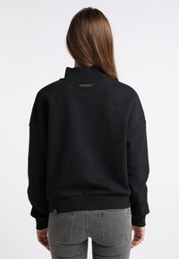 Musta pusero, jossa on korkea kaulus, lasketut olkapäät sekä resorireunukset hihoissa ja helmassa. Selässä pieni merkitty merkintä.