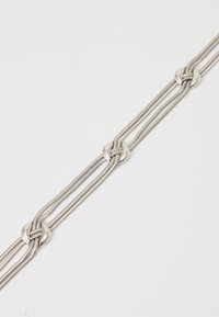 Zilveren ketting met drie ronde sluitingen, elk met meerdere dunne verknopte kettingen, weergegeven op een witte achtergrond.