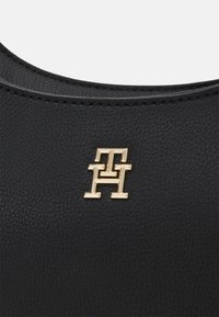 Czarna torebka z teksturowanej skóry z wyraźnym monogramem w złotym odcieniu o geometrycznym wzorze. Gładkie, zaokrąglone krawędzie podkreślają jej kształt.