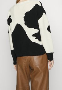 Pull tricoté à motif noir et blanc, coupe ample, avec un col rond et un ourlet côtelé, associé à un pantalon en cuir marron.