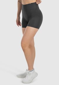 Hoge zwarte sportshorts met een gladde textuur, een aansluitend ontwerp en minimale naden, gecombineerd met witte sportschoenen.