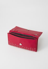 Portefeuille en cuir rouge avec une finition brillante, ornée de clous en argent le long du bas, fermé par un bouton pression et doté d'une poche zippée.