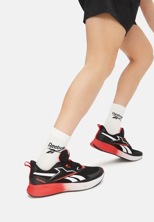 Melni un sarkani sporta apavi ar baltu akcentu, ar strukturētu zoli un šņorēšanas dizainu. Valkāti ar baltām Reebok zeķēm.