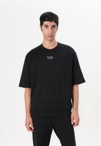 Sweatshirt noir oversize en mélange de coton, avec un col rond et des manches courtes. Détail de logo sur le devant en argent.
