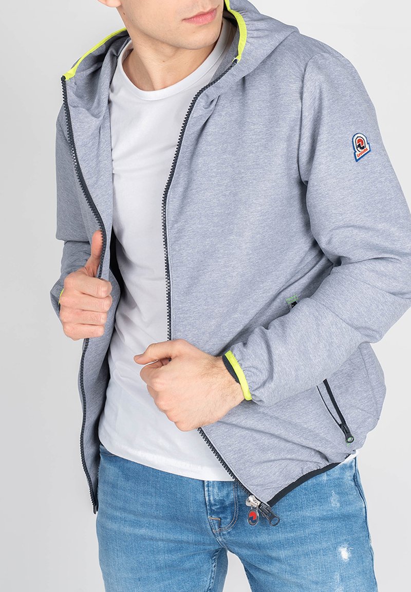 Grå zip-up jakke med hætte, der har en lys gul indvendig foring og lynlåsede lommer, lavet af et letvægtsmateriale.
