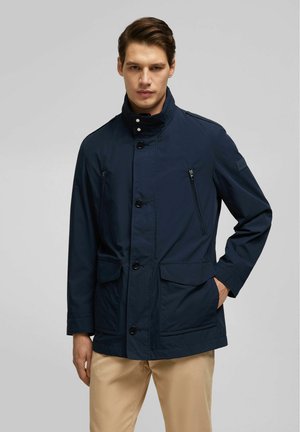 Marineblaue wasserdichte Jacke mit hohem Kragen, vorderen Knöpfen, zwei mit Reißverschluss versehenen Brusttaschen und zwei vorderen Klapptaschen. Glatte Textur.