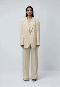 Kermavaate pinstripe-puku, joka koostuu löysästi istuvasta bleiseristä leveillä liittymillä ja vastaavista housuista, joissa on napitettu etuosa.