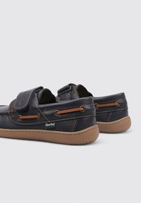 Zapatos de cuero azul oscuro con suela de goma, que presentan acentos marrones, una correa de gancho y bucle, y costuras decorativas en los laterales.