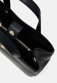 Navy Lederhandtasche mit doppelten Tragegriffen, goldenen Beschlägen und einem innen liegenden Reißverschlussfach. Glatte Textur und minimalistisches Design.