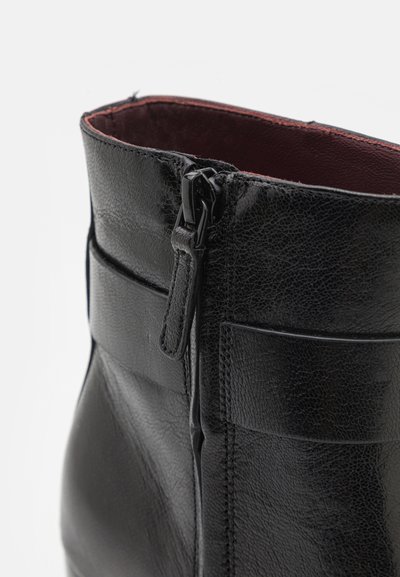 Stivale alla caviglia in pelle nera con chiusura a zip, superficie texturizzata e foderato in bordeaux. Cuciture dettagliate evidenti lungo i lati.