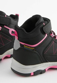 Scarponi da trekking neri con dettagli rosa, caratterizzati da una tomaia testurizzata, colletto imbottito e etichetta HydroGuard impermeabile sul tallone.