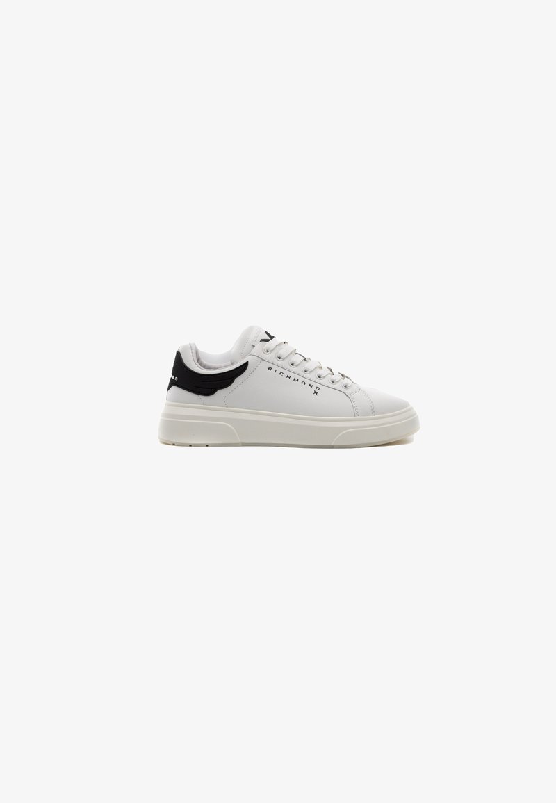Zapatilla blanca con parte superior de cuero texturizado, acento negro en el talón y suela blanca plana. Presenta un logotipo y un cierre tradicional con cordones.