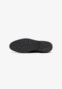 Semelle de chaussure noire en caoutchouc texturé, présentant des motifs circulaires en relief pour une meilleure adhérence. Bout arrondi et bords lisses. Taille indiquée comme 45.