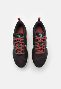 Svarta sportskor med texturerad mesh-överdel, röda accenter och snören. Har mintgröna logotyper och en vit sula.