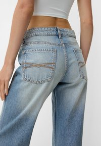 Lyseblå denim jeans med høj talje, der har en afslappet pasform, kontrasterende syninger og to baglommer med et unikt krydsmønster.