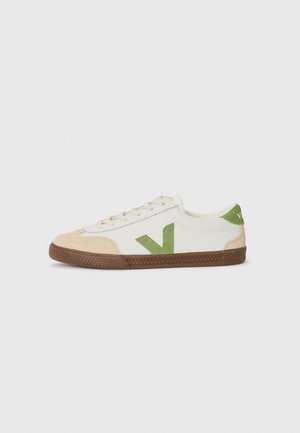 White canvas sneaker with tan suede toe cap, green suede logo accent, and brown rubber sole. Classic lace-up design.