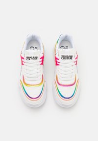 White sneakers with colorful stitching in rainbow hues, featuring a textured upper, round toe, and flat laces. Branding on tongue.