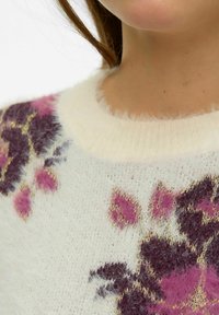 Pūkains balts džemperis ar rozā un violetām ziedu rakstiem, ar ribotu apkakli un mīkstu, teksturētu apdari.