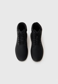 Botas altas negras con un acabado suave, que presentan cordones redondos, ojales de metal y una suela de goma texturizada para mayor agarre.