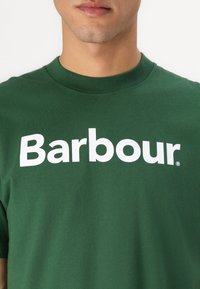 Πράσινο βαμβακερό μπλουζάκι με κοντά μανίκια που διαθέτει ένα μεγάλο λευκό λογότυπο "Barbour" στο κέντρο, και κλασικό σχέδιο γύρω από τον λαιμό.