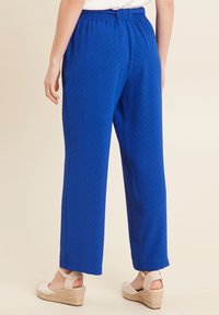 Blauwe, gestructureerde, wijdvallende broek met een elastische tailleband, voorzien van een subtiel patroon. Gecombineerd met lichtgekleurde sleehakken.