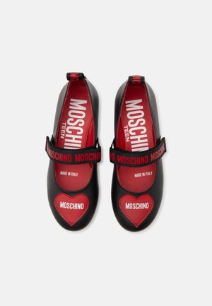 Chaussures Mary Jane noires avec des patchs en forme de cœur rouges étiquetés Moschino et des semelles intérieures rouges avec la marque Moschino Teen.