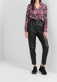 Blusa nera a maniche lunghe con fiori rosa e rossi, abbinata a pantaloni in pelle neri a vita alta e sneakers nere.