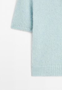 Light blue soft knitted sweater sleeve and side detail on a white background.