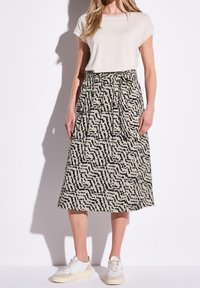 Beige midi-kjol med mönster i svart abstrakt design, med en plisserad framsida och ett elastiskt midjeband. Matchad med vita sneakers.