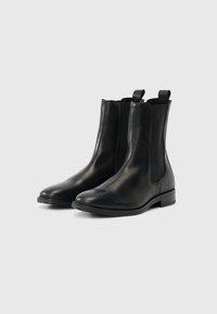Černé kožené chelsea boty mají elastické boční panely, zaoblenou špičku a táhla na zapínání, s hladkým povrchem a nízkým naskládaným podpatkem.