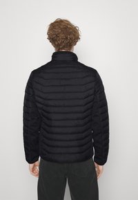 Sort pufferjakke med ribbet quilting, høj krave og håndledsmanchetter. Har glat stof og en tætsiddende design. Ensfarvet bagudblik.