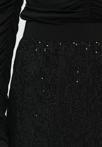 Sort pailetteret nederdel med teksturerede lodrette plisseringer, der har en solid elastisk talje. Stoffet har en subtil glans og varieret lysrefleksion.