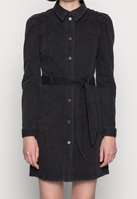 Robe en denim noir à manches longues, fermeture à boutons sur le devant et ceinture à nouer à la taille. Présente un col et des détails de couture discrets.