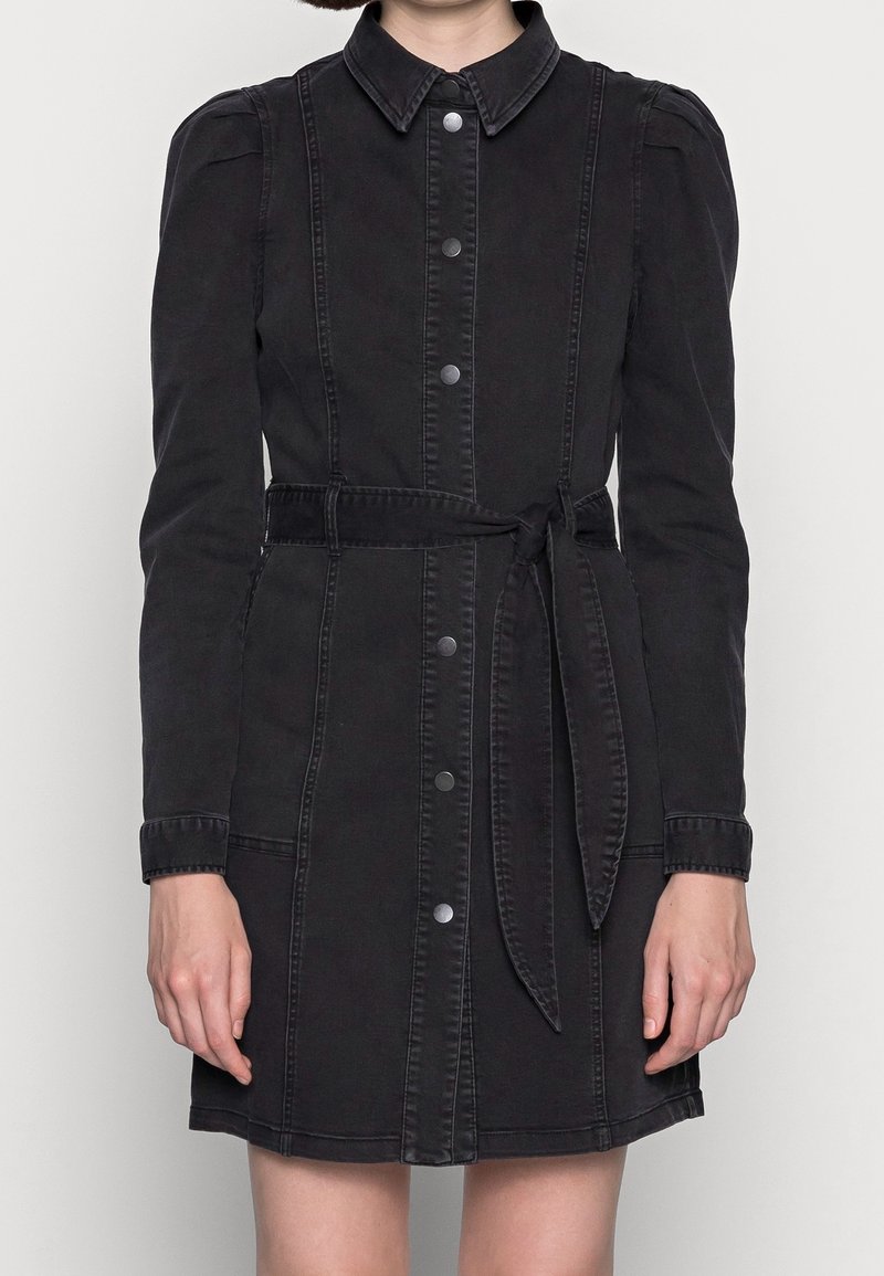 Robe en denim noir à manches longues, fermeture à boutons sur le devant et ceinture à nouer à la taille. Présente un col et des détails de couture discrets.