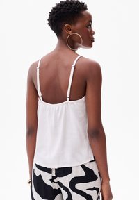 Witte mouwloze top met verstelbare bandjes, geplooide achterkant en lichtgewicht stof. Gecombineerd met zwart-witte gefacetteerde broek.