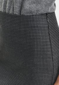 Jupe à motif pied-de-poule noir et gris, en tissu texturé, avec une silhouette ajustée et un détail de fermeture éclair sur le côté.