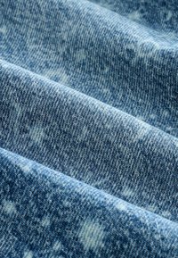 Tessuto in denim con un sottile motivo sbiadito azzurro chiaro, che mostra una trama testurizzata e variazioni di colore tra blu chiaro e blu scuro in primo piano.