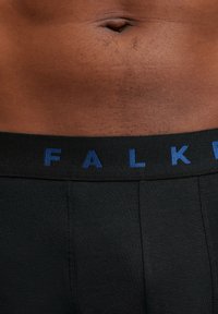 Black underwear with a textured waistband featuring blue "FALK" lettering. The fabric appears smooth and fitted, emphasizing the minimalist design.