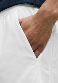 Bermudas deportivas blancas con cintura elástica y bolsillo lateral, con una textura de tela suave y un sutil detalle de costura.