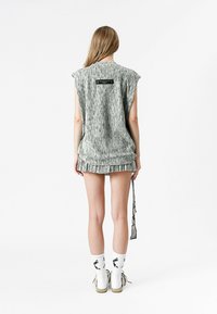 Top sin mangas de color gris con estampado y dobladillo deshilachado, combinado con pantalones cortos a juego. Presenta una etiqueta en la parte de atrás. Los accesorios incluyen calcentines y zapatos blancos.