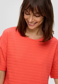 Koraalroze t-shirt met een ronde hals en korte mouwen, voorzien van subtiele horizontale ribbels voor extra diepte.