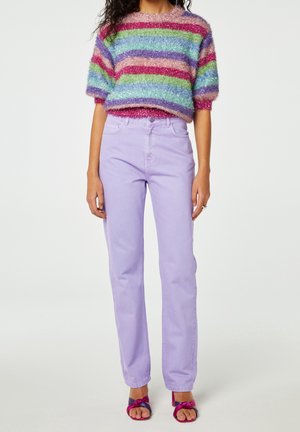 Kobieta ubrana w miękki, wielokolorowy sweter w paski z krótkim rękawem, lawendowe dżinsy z wysokim stanem oraz fioletowo-różowe sandały na odkryte palce.