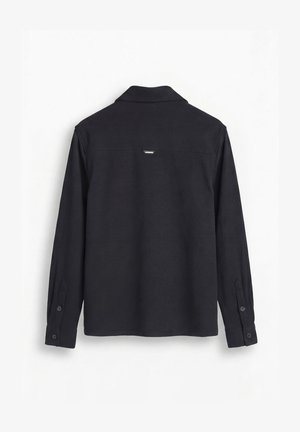 Camisa negra de manga larga mostrada desde atrás, con cuello, puños abotonados y un pequeño detalle reflectante debajo del cuello.