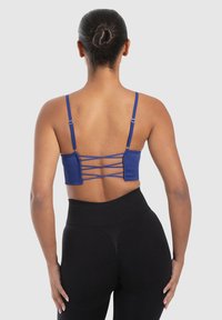 Bralette de tejido acanalado azul con tirantes ajustables y un diseño entrecruzado en la parte posterior. Combinado con leggins negros de cintura alta.