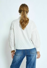 Witte blouse met gestructureerde stippen, opgezette mouwen en een kraag, gecombineerd met blauwe high-waisted jeans. Eenvoudig en elegant ontwerp.