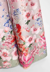 Tissu fluide avec un motif floral multicolore en nuances de rose, rouge, violet et vert, couvrant partiellement un pied dans une chaussure à bout ouvert.