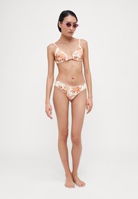 Květinový bikini set v jemných oranžových a smetanových barvách, trojúhelníková podprsenka s nastavitelnými ramínky a odpovídající nízké bikini kalhotky.
