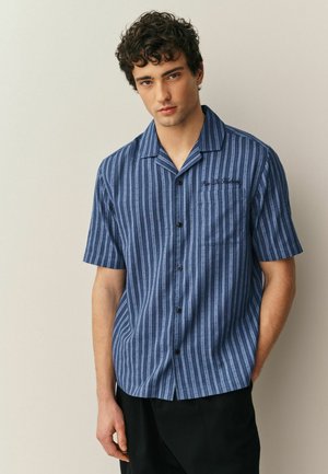 Kurzärmeliges blaues Hemd mit vertikalen Streifen, strukturierter Stoff, Knopfleiste vorne und einer Brusttasche mit dezentem schwarzem Stickereimotiv.