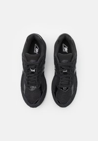 Crne atletske tenisice s teksturiranim gornjim dijelom od tkanine, s crnim vezicama, mekanim potplatom i reflektirajućim detaljima. Vidljiv New Balance logo.