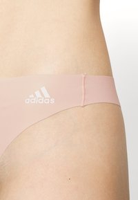 Lichtroze string met een gladde textuur, voorzien van een wit Adidas-logo op de tailleband. Het ontwerp is minimalistisch en lichaamsvormend.
